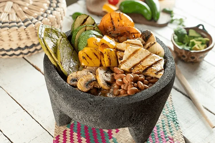 Molcajete bowl filled with grilled chicken, vegetables, and beans.
