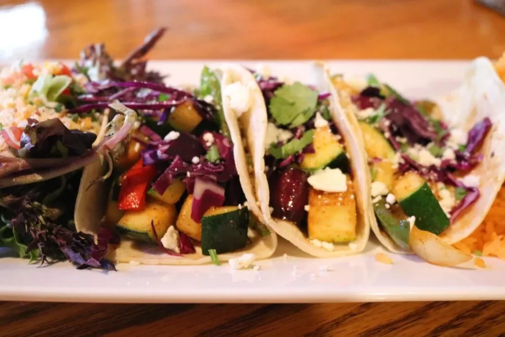 Close-up: three colorful vegetable tacos with cheese and herbs.