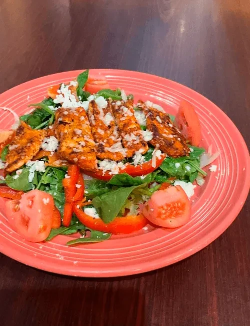 Grilled chicken salad with cheese, vegetables on a reddish-orange plate.