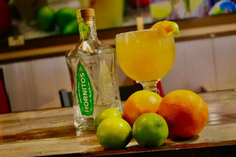 Hornitos tequila, margarita, citrus fruits on a rustic bar top.