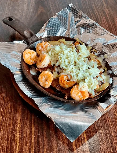Sizzling shrimp and melted cheese in a cast-iron skillet on a wooden board.