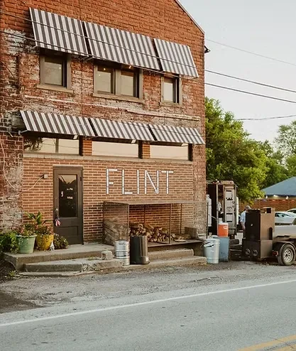 FLINT restaurant exterior: brick building, awnings, firewood, outdoor smoker.