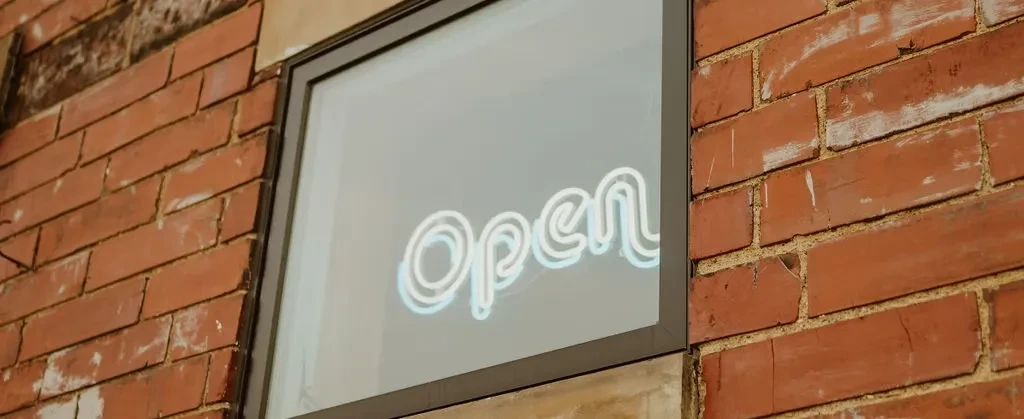 A white "Open" neon sign glows in a weathered brick wall window.