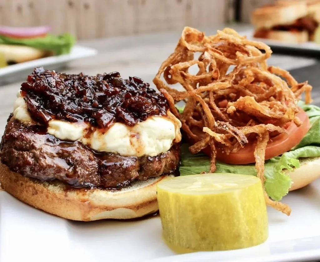 Open-faced gourmet burger with cheese, caramelized onions, lettuce, tomato, fried onions.
