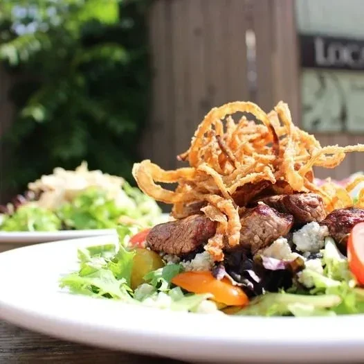 Steak salad with blue cheese, mixed greens, tomatoes, crispy onions outdoors.