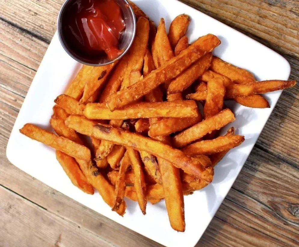 Golden-brown sweet potato fries, ketchup, white plate, wooden table.