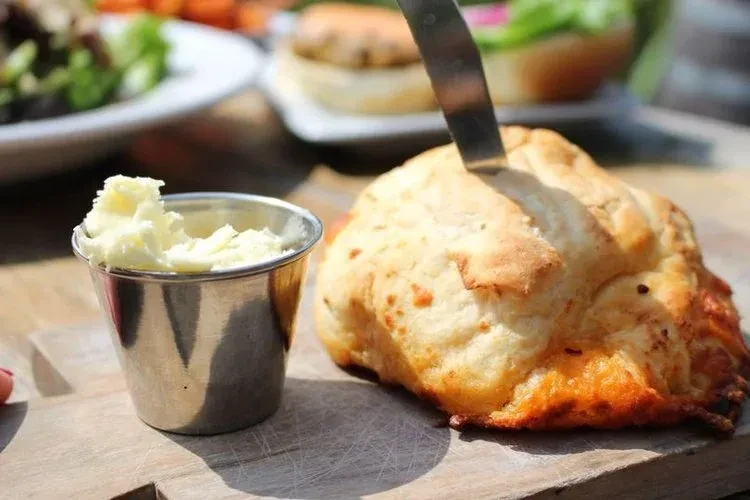 Golden baked good with knife, butter cup, on a wooden board.