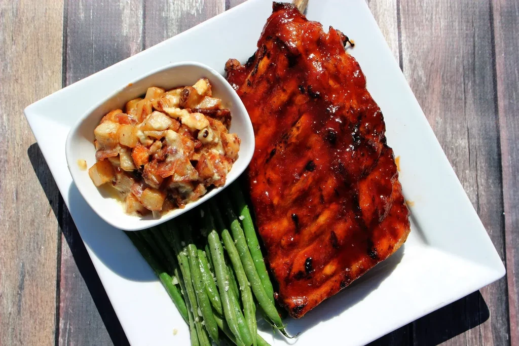 Glossy barbecued ribs, roasted potatoes, and green beans on a white plate.