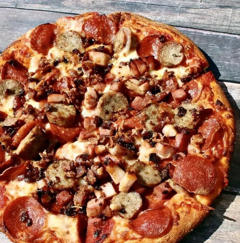 Freshly baked meat pizza with pepperoni and sausage on a rustic wood surface.
