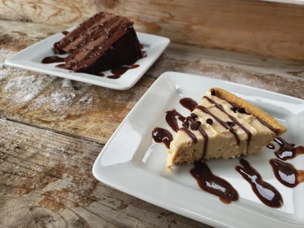 Two dessert slices: chocolate-drizzled pie and layered chocolate cake on wood.