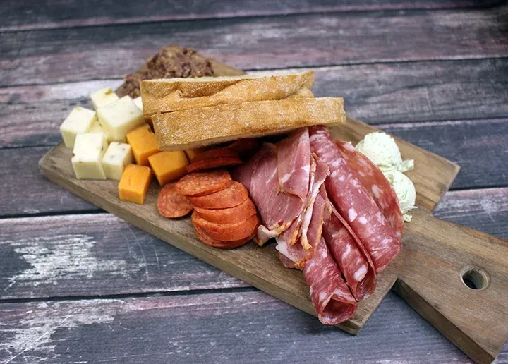Sliced meats, cheeses, bread, and spreads on a rustic charcuterie board.