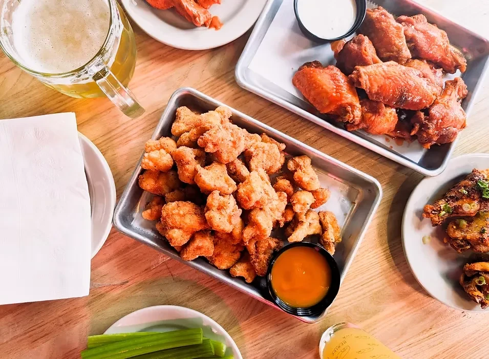 Overhead view of fried chicken wings, boneless chicken, beer, and celery.