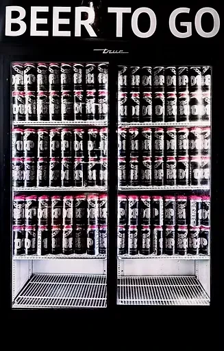 Black two-door refrigerator with "BEER TO GO" sign and stacked beer cans.