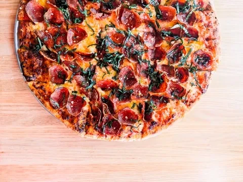 Overhead cooked pepperoni pizza with green herbs on wood.