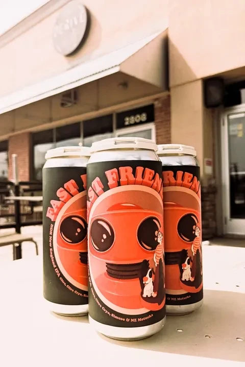 Three dark "FAST FRIEND" IPA cans on a table outside building 2808.