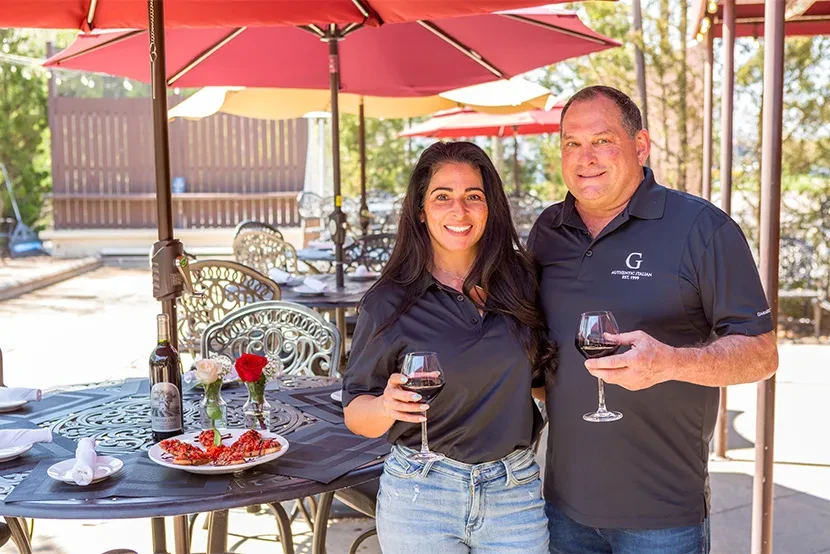 Smiling couple with wine glasses at outdoor "G AUTHENTIC ITALIAN" restaurant.