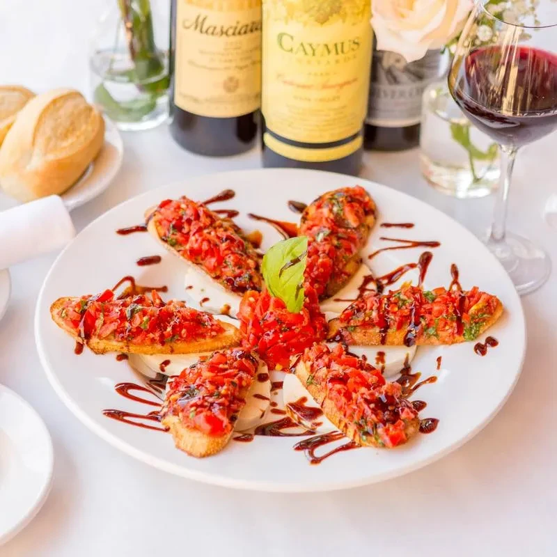 Close-up of bruschetta with tomatoes, herbs, balsamic, mozzarella on plate.