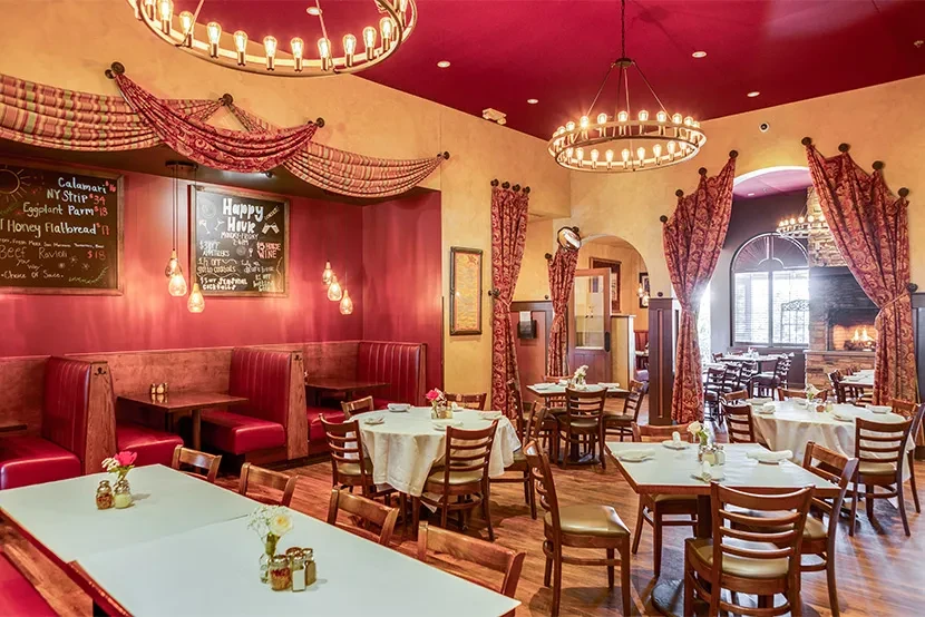 Restaurant dining room with red booths, tables, and ornate chandeliers.