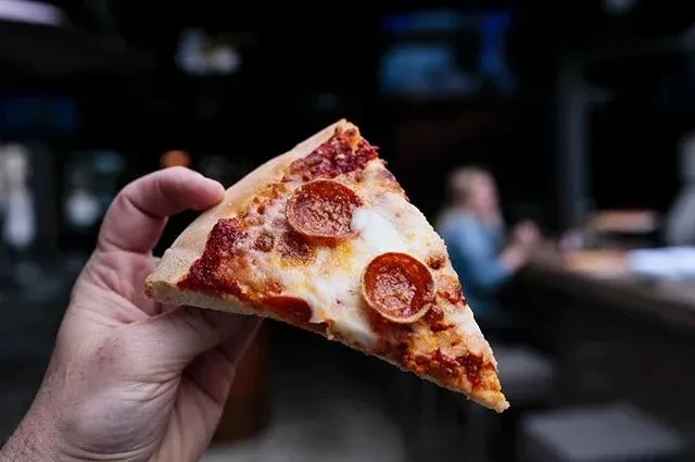 Hand holding a crisp pepperoni pizza slice with melted cheese.