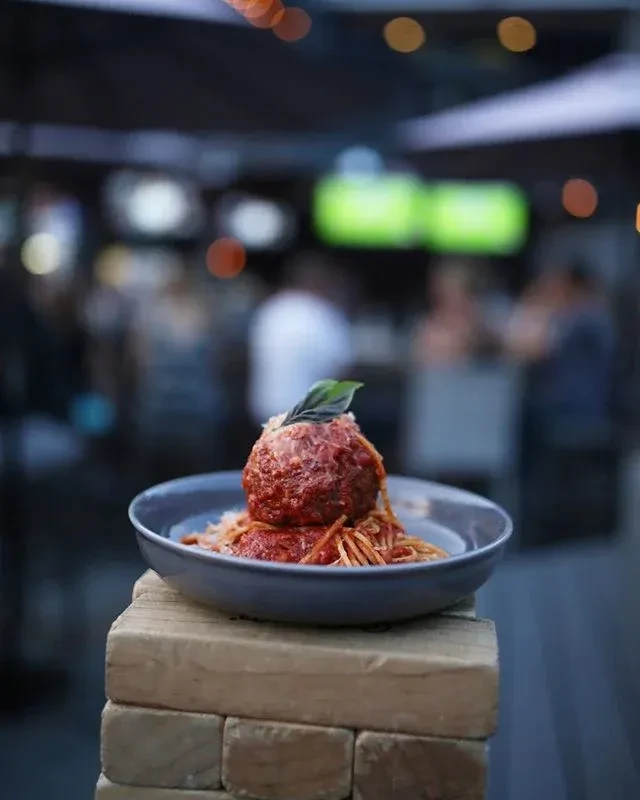 Close-up of spaghetti and a meatball topped with cheese and basil.