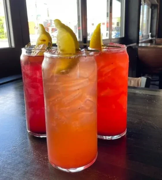 Three colorful, iced cocktails in can-shaped glasses with lemon.