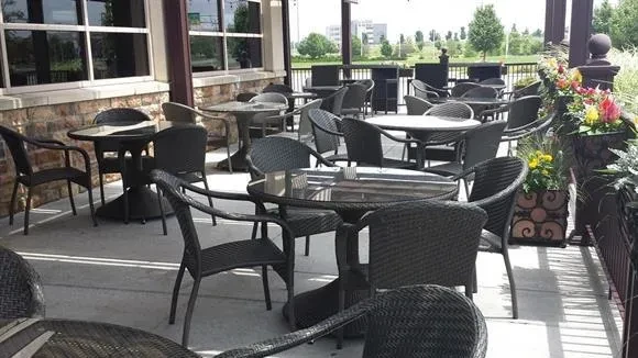 Empty outdoor patio with dark wicker chairs and colorful flowers.