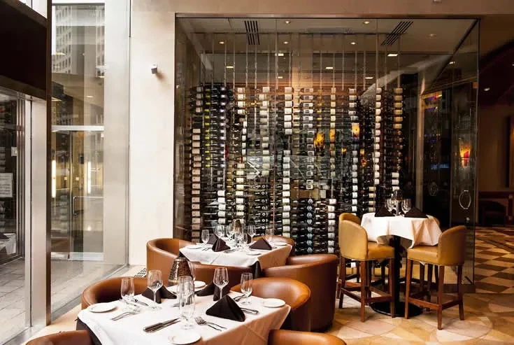 Upscale restaurant interior with set tables and a massive glass wine wall.