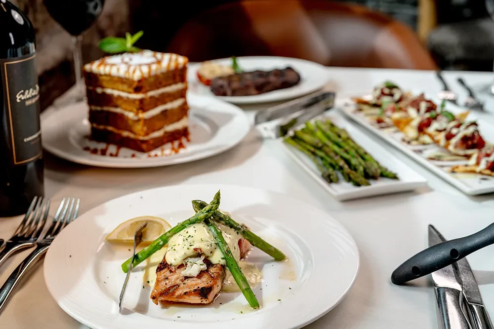 Upscale dining table with grilled salmon, cake, wine, and gourmet food.