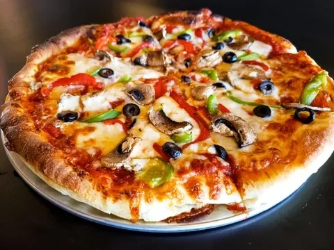 Sliced pizza with cheese, olives, bell peppers, and mushrooms on a pan.