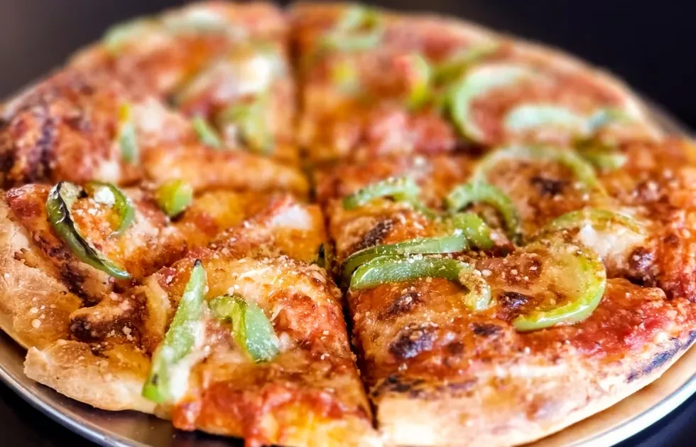 Freshly baked pizza with cheese, green peppers, and pepperoni on a pan.