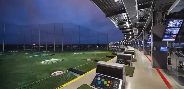 Illuminated multi-level golf driving range with hitting bays and targets at night.
