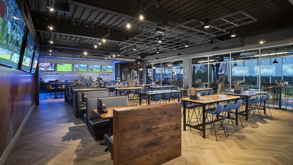 Modern sports bar interior, varied seating, multiple screens, golf range view.