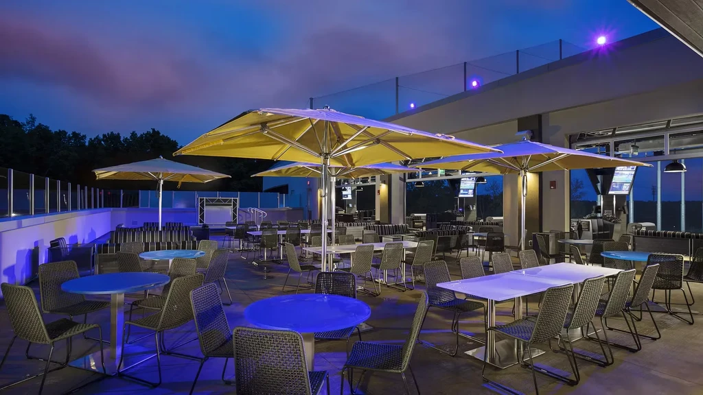 Empty outdoor dining patio at night with yellow umbrellas and blue lighting.