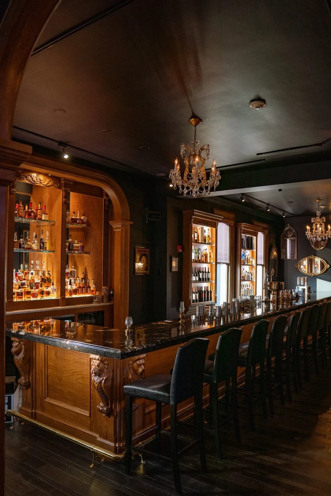 Ornate wooden bar, dark marble, illuminated liquor shelves, crystal chandeliers.