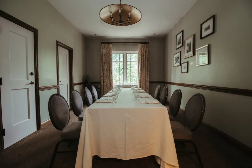 Long private dining room with a set table, chandelier, and window.