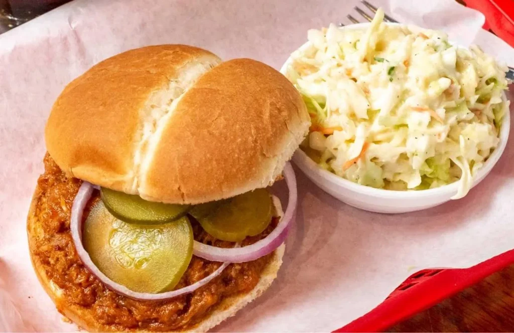 Sloppy joe sandwich with pickles, red onion, and a side of coleslaw.