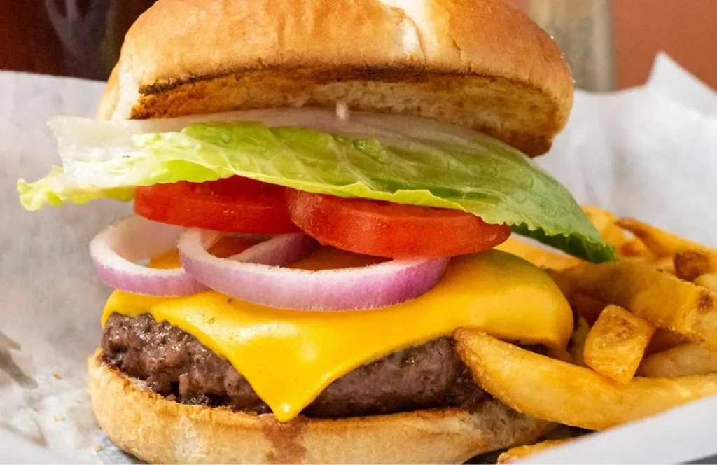 Close-up of a cheeseburger with melted cheese and wedge fries.