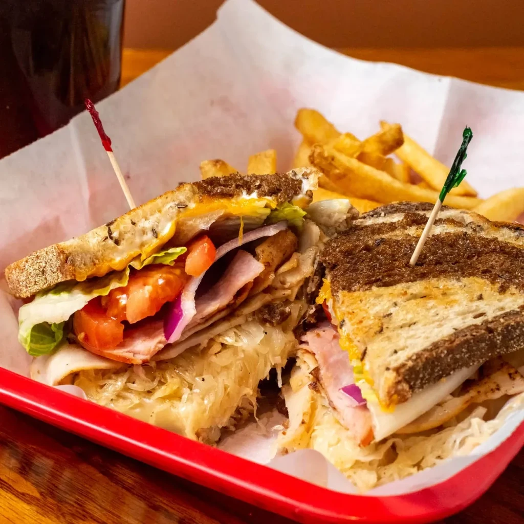 Close-up of a large multi-layered deli sandwich in a red basket.