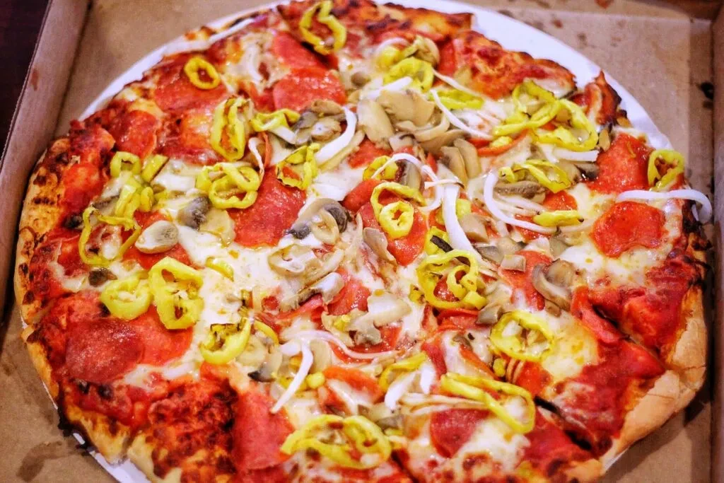 A whole pepperoni, mushroom, onion, and banana pepper pizza in a box.