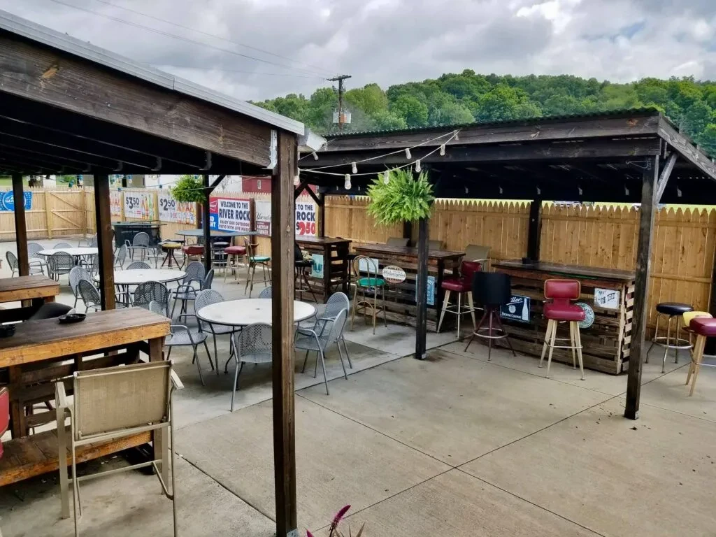 Outdoor restaurant patio with pergolas, colorful stools, and a "River Rock" sign.