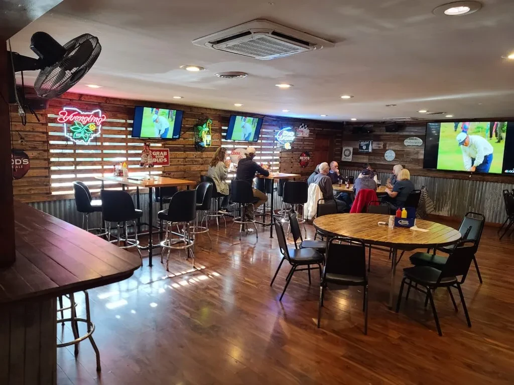 Rustic casual bar interior with wooden walls, neon signs, and patrons.