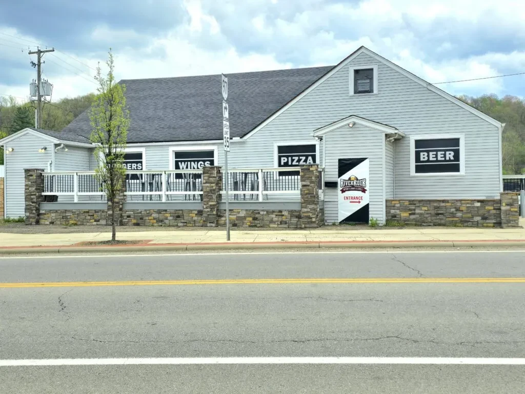 Single-story restaurant with stone facade, gray siding, and menu signs.