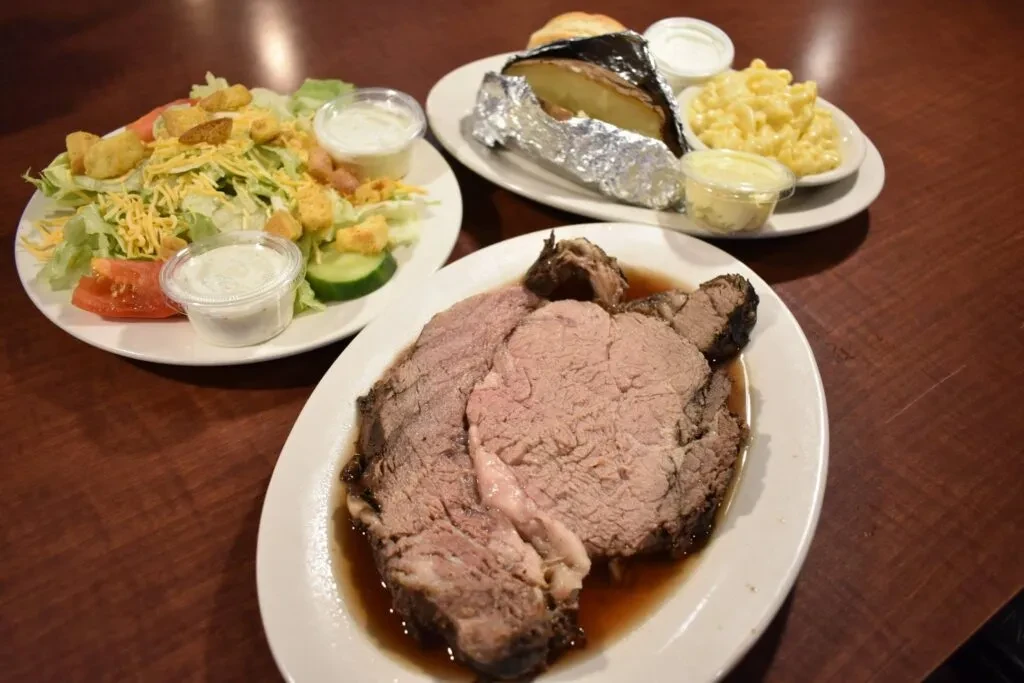 Three plates of prime rib, garden salad, and baked potato.