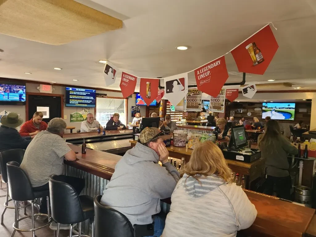 Busy bar with patrons, TVs showing sports, and baseball pennants.