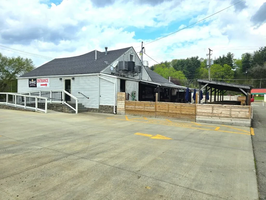 Grey restaurant building with an "ENTRANCE" sign, ramp, and outdoor patio.