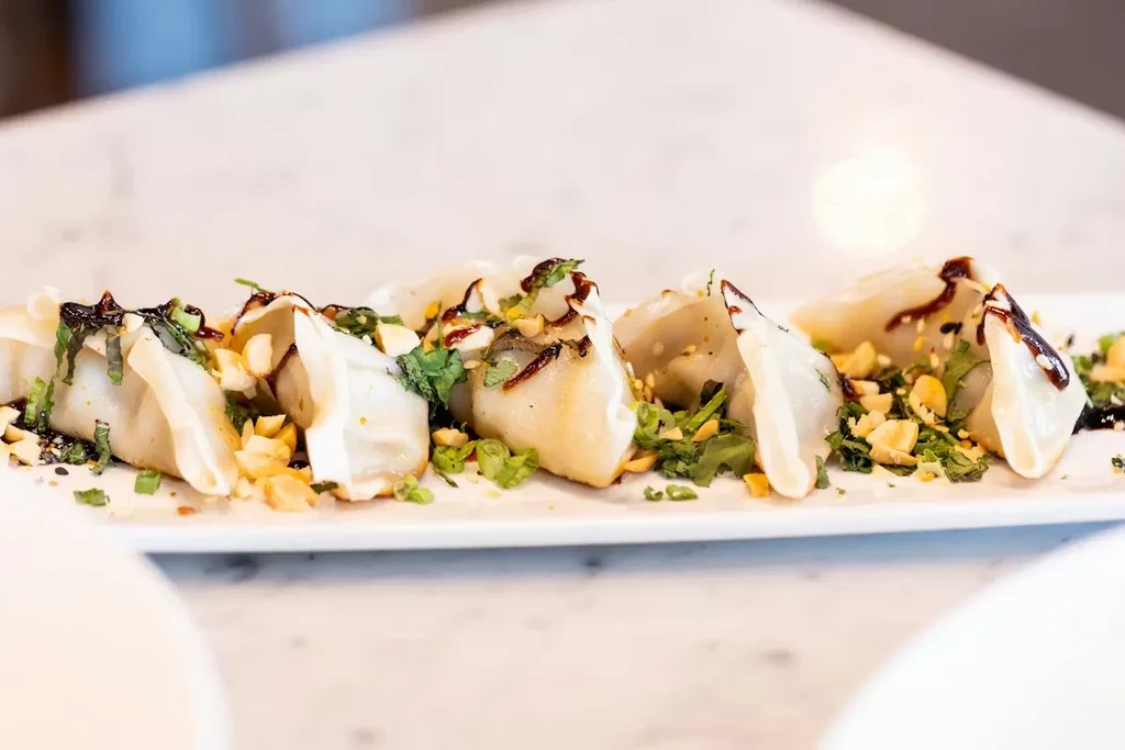 Golden pan-fried dumplings with peanuts, green herbs, and dark sauce.