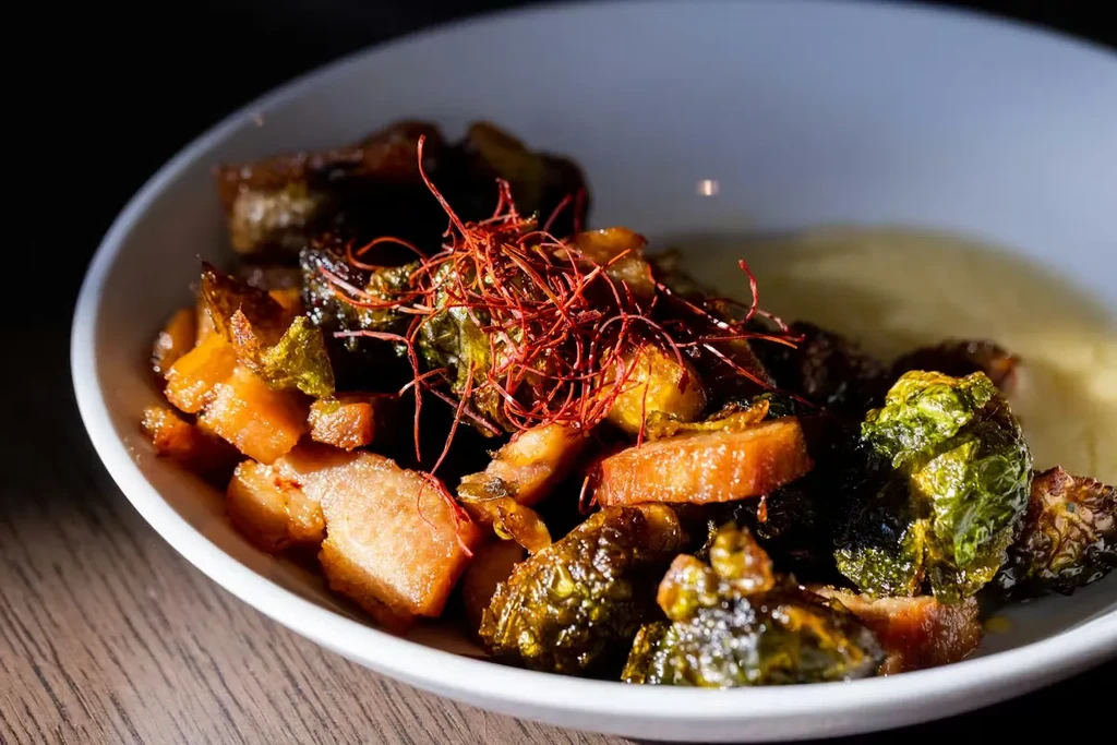 Roasted vegetables, meat, red threads, yellow sauce in a bowl.