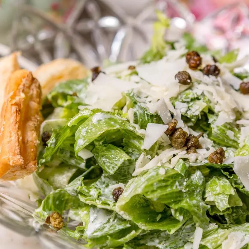 Close-up of fresh salad: lettuce, creamy dressing, Parmesan, capers, crouton.