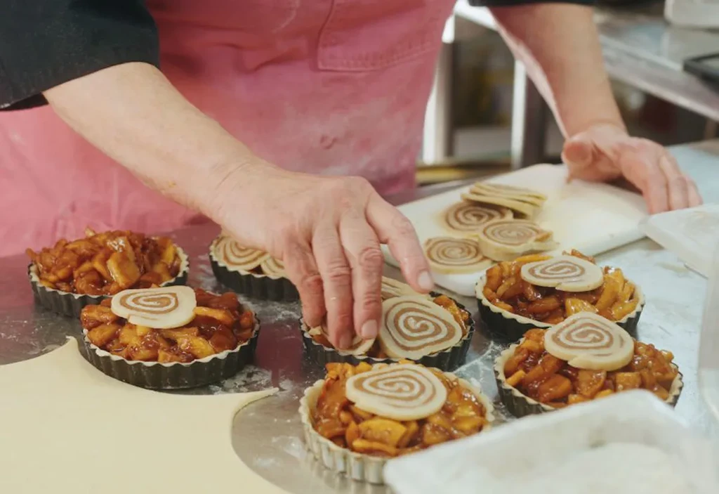 Hands decorating mini apple tarts with pastry spirals.