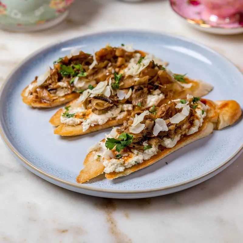 Three crostini with mushrooms, creamy cheese, and parsley on a blue plate.